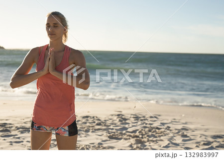 Woman standing on sandy beach at water's edge wearing coral tank top, patterned shorts, copy space 132983997