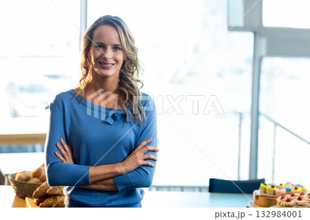 Woman wearing blue sweater standing behind counter in bakery with wicker bread basket and cupcakes 132984001