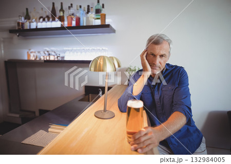 Sitting senior man holding pint of beer, resting head on hand at bar counter, copy space Sitting senior man holding pint of beer, resting head on hand at bar counter, copy space 132984005