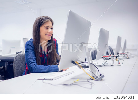 Female student smiling while using computer monitor and keyboard in computer lab, copy space Female student smiling while using computer monitor and keyboard in computer lab, copy space 132984031