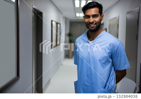Asian male nurse standing in hospital corridor wearing light blue scrubs by closed doors Asian male nurse standing in hospital corridor wearing light blue scrubs by closed doors 132984038