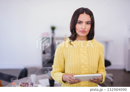 Woman standing in modern office holding white tablet while scanning magazines on desk 132984090