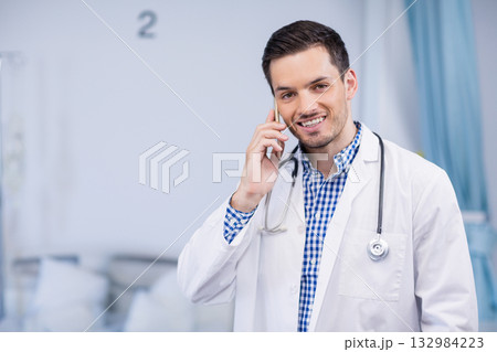 Chinese male doctor talking on smartphone near hospital bed with stethoscope, copy space 132984223