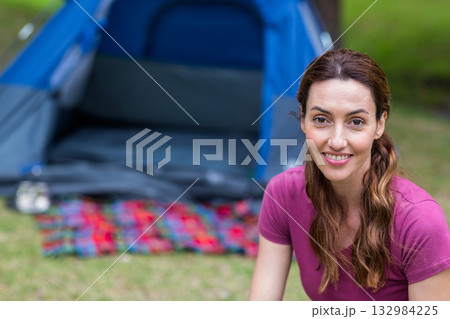 Woman sitting on grass in front of blue camping tent on multicolored plaid blanket, copy space 132984225