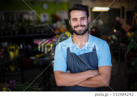 Man standing with crossed arms by wooden display tables in flower shop arranging colorful bouquets 132984242