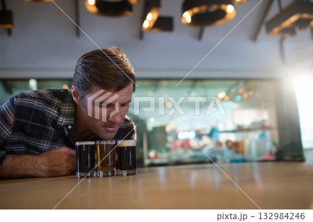 Man leaning over bar counter in brewery taproom inspecting beer flight under warm lights 132984246