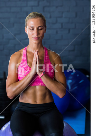 Female athlete balancing on purple ball wearing pink bra and black leggings by plates at gym Female athlete balancing on purple ball wearing pink bra and black leggings by plates at gym 132984256