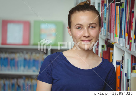 Female teenager leaning against bookshelf in library aisle browsing colorful books and artwork Female teenager leaning against bookshelf in library aisle browsing colorful books and artwork 132984320