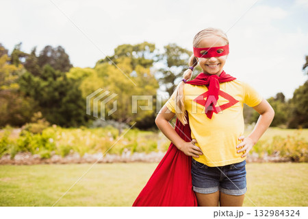 School-age girl wearing red eye mask and cape standing in park on sunny day, copy space 132984324