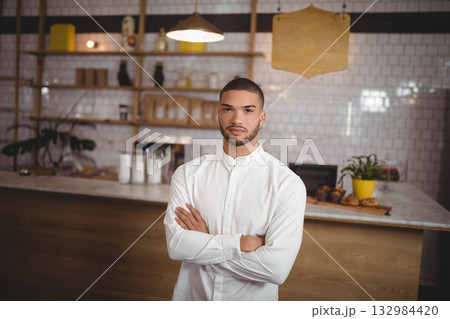Man wearing white shirt standing behind marble-topped café counter with shelves displaying pastries Man wearing white shirt standing behind marble-topped café counter with shelves displaying pastries 132984420