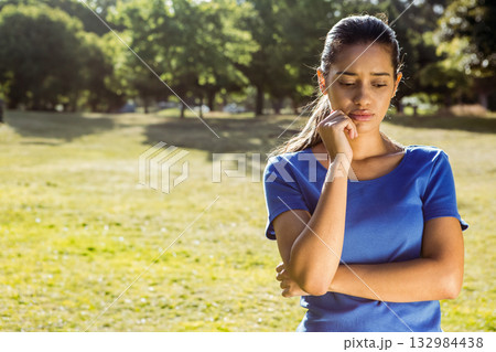 Asian woman standing in sunlit park, resting chin on hand while surveying grassy field, copy space Asian woman standing in sunlit park, resting chin on hand while surveying grassy field, copy space 132984438
