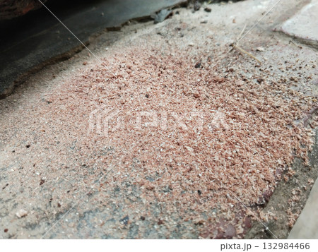 Fresh wood sawdust scattered on ground after cutting tree trunk with hand saw, close-up texture showing natural wooden particles from carpentry or tree-cutting activity 132984466