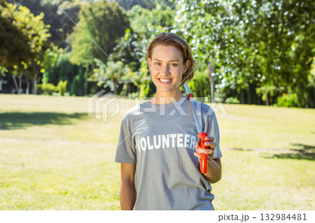 Smiling woman standing in open park wearing VOLUNTEER t-shirt and holding red litter picker tool Smiling woman standing in open park wearing VOLUNTEER t-shirt and holding red litter picker tool 132984481