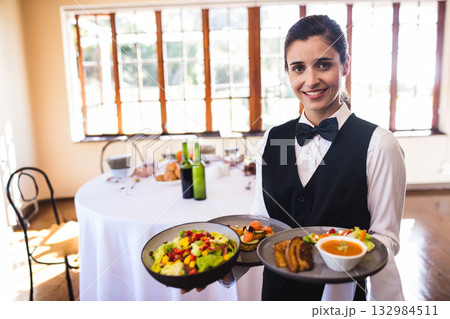 Female server holding trays laden with salad soup bread appetizers in banquet hall, copy space Female server holding trays laden with salad soup bread appetizers in banquet hall, copy space 132984511
