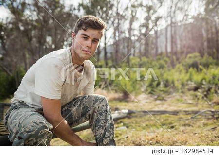 Man in his twenties tying boots on bench wearing camouflage trousers at forest edge, copy space Man in his twenties tying boots on bench wearing camouflage trousers at forest edge, copy space 132984514