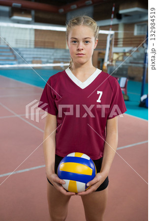 Teenage female standing at volleyball net in gym, holding volleyball by waist in jersey number 7 Teenage female standing at volleyball net in gym, holding volleyball by waist in jersey number 7 132984519