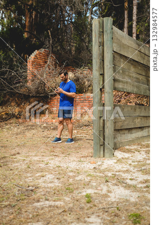 Man wearing blue gear climbing wooden obstacle wall outdoors beside collapsed wall with earphones Man wearing blue gear climbing wooden obstacle wall outdoors beside collapsed wall with earphones 132984577