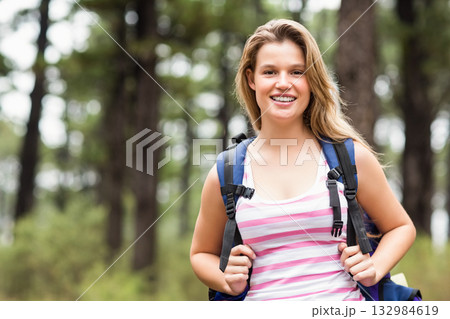 Woman wearing sleeveless pink striped top smiling at camera in pine forest holding hiking backpack Woman wearing sleeveless pink striped top smiling at camera in pine forest holding hiking backpack 132984619