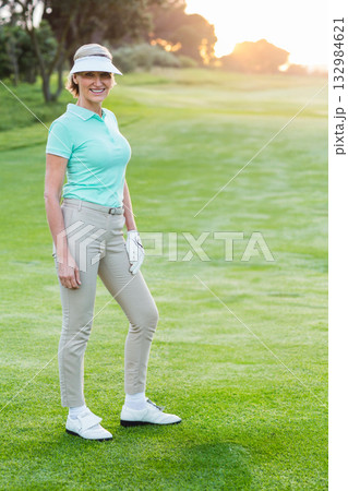 Senior woman standing on golf fairway at sunset wearing visor, golf glove, golf shoes, copy space Senior woman standing on golf fairway at sunset wearing visor, golf glove, golf shoes, copy space 132984621