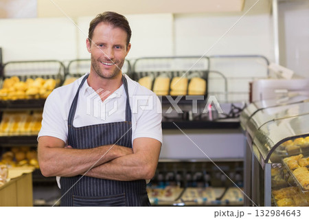 Man wearing pinstriped apron standing in bakery shop among bread loaves and pastries Man wearing pinstriped apron standing in bakery shop among bread loaves and pastries 132984643