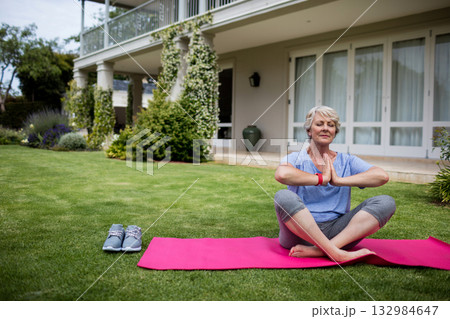 Senior woman wearing fitness tracker stretching on pink mat in front yard with shoes, copy space 132984647
