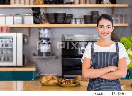 Female barista standing behind wooden counter displaying pastry trays and rolls at cafe, copy space 132984652
