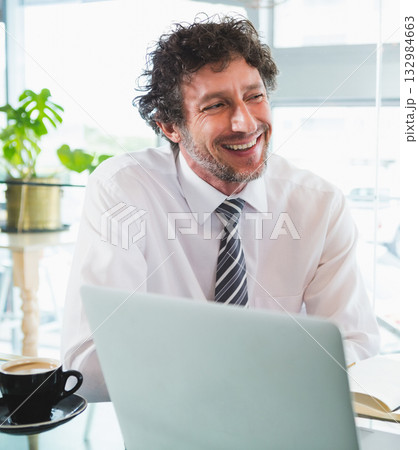Mature man in business attire working on laptop at workspace by window with coffee cup, notebook Mature man in business attire working on laptop at workspace by window with coffee cup, notebook 132984663