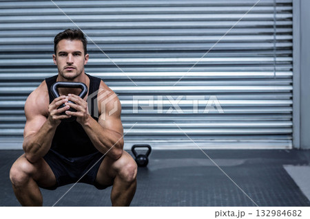 Mid adult man wearing sportswear doing kettlebell squat on gym mat with metal door, copy space 132984682