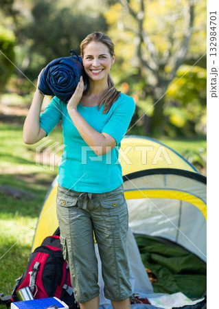 Mid adult woman wearing turquoise shirt holding sleeping bag at campsite with tent and backpack Mid adult woman wearing turquoise shirt holding sleeping bag at campsite with tent and backpack 132984701