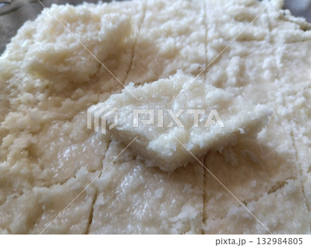 Closeup of traditional Indian coconut halwa made with grated nariyal, evenly spread and textured with knife marks, with a visible square slice placed on top of the sweet Closeup of traditional Indian coconut halwa made with grated nariyal, evenly spread and textured with knife marks, with a visible square slice placed on top of the sweet 132984805