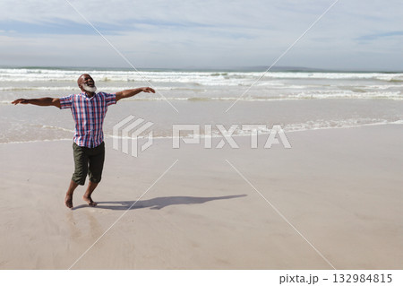 African American man stretching arms on beach wearing rolled-up pants barefoot with waves rolling African American man stretching arms on beach wearing rolled-up pants barefoot with waves rolling 132984815