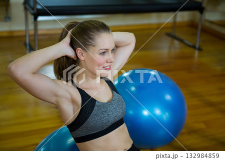 Female athlete balancing core muscles on blue stability ball near workout bench in fitness studio 132984859