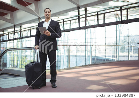 Businessman in suit holding tablet standing on airport escalator with rolling suitcase, copy space Businessman in suit holding tablet standing on airport escalator with rolling suitcase, copy space 132984887