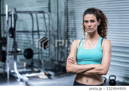 Female trainer standing arms crossed in gym by squat rack wearing workout attire, copy space Female trainer standing arms crossed in gym by squat rack wearing workout attire, copy space 132984909