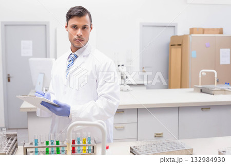 Male scientist recording on clipboard at lab bench near test tubes and microscope 132984930