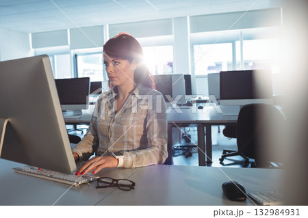 Female professional using keyboard and mouse at desk in computer lab with monitor and eyeglasses 132984931