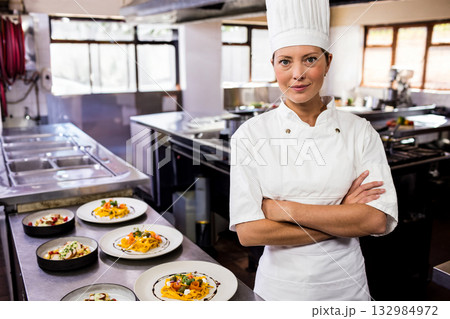 Female chef standing beside prep table in kitchen showcasing plated pasta and salads, copy space Female chef standing beside prep table in kitchen showcasing plated pasta and salads, copy space 132984972