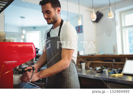 Male barista operating red espresso machine portafilter on counter at coffee shop using tablet Male barista operating red espresso machine portafilter on counter at coffee shop using tablet 132984995