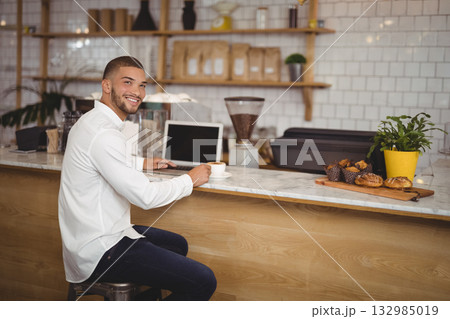 Man sitting on stool at cafe countertop, typing on laptop, sipping coffee near pastries, copy space Man sitting on stool at cafe countertop, typing on laptop, sipping coffee near pastries, copy space 132985019