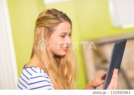 Teenage girl wearing striped long sleeve top holding tablet and looking at screen at home 132985061