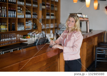 White female standing at bar counter holding wine glass under lights by bottle shelves, copy space White female standing at bar counter holding wine glass under lights by bottle shelves, copy space 132985080