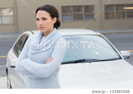 Woman standing with arms crossed wearing knit sweater on urban sidewalk in front of parked sedan Woman standing with arms crossed wearing knit sweater on urban sidewalk in front of parked sedan 132985088