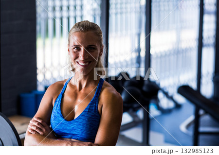 Woman trainer smiling and crossing arms at gym near medicine balls in blue tank top 132985123
