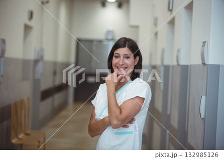 Female nurse standing and smiling in hospital corridor with wooden chairs and double doors Female nurse standing and smiling in hospital corridor with wooden chairs and double doors 132985126