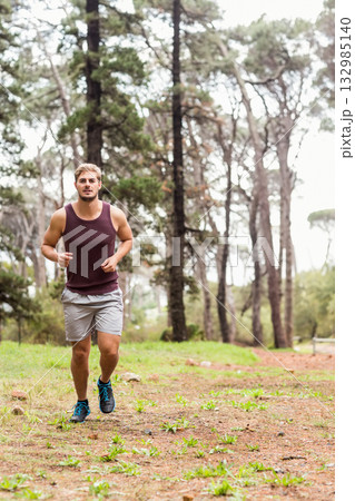 Male runner jogging along narrow pine forest trail wearing maroon athletic tank and running shoes Male runner jogging along narrow pine forest trail wearing maroon athletic tank and running shoes 132985140