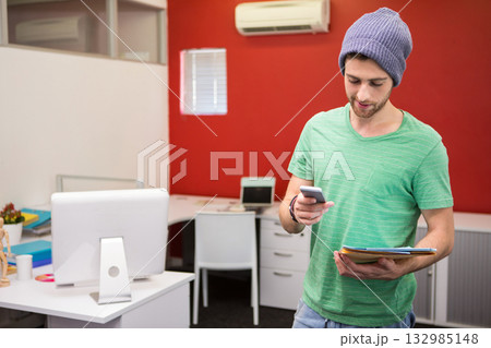 Man holding smartphone while checking messages in office with red wall, tablet monitor, copy space Man holding smartphone while checking messages in office with red wall, tablet monitor, copy space 132985148