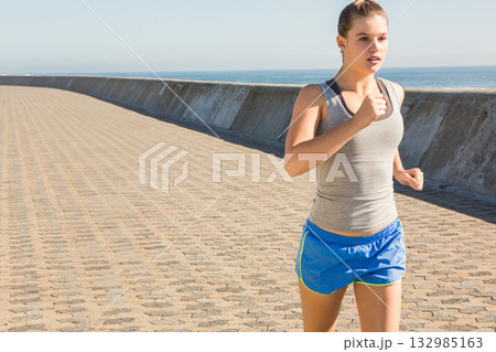 Female runner jogging along coastal walkway wearing gray tank top and blue shorts, copy space 132985163