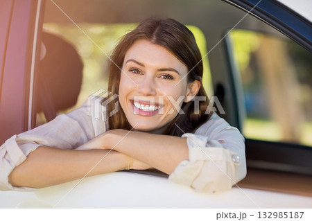 Woman leaning out car window wearing light-colored shirt on sunny suburban street by white car door 132985187