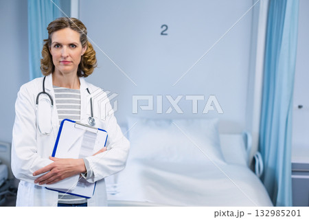 Female doctor in 40s holding clipboard and pen wearing stethoscope in hospital room, copy space 132985201