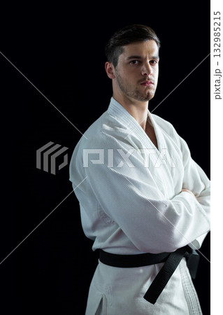 Male martial artist wearing white gi, black belt in studio against black backdrop looking serious Male martial artist wearing white gi, black belt in studio against black backdrop looking serious 132985215
